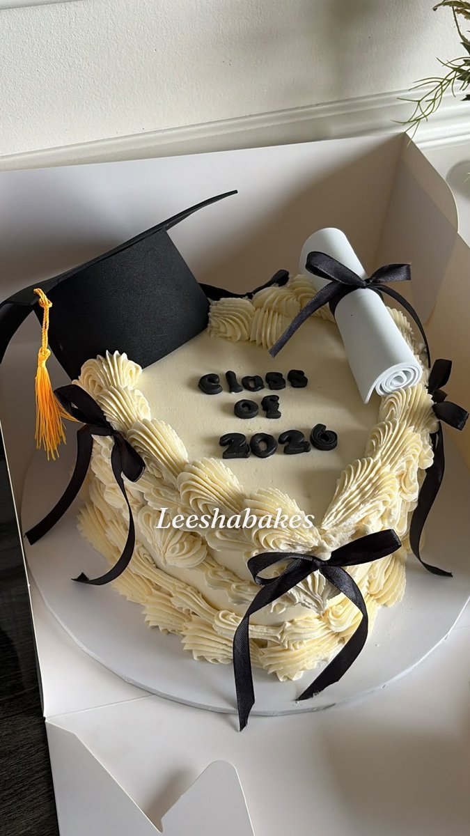 Cream graduation cake with black bows, a graduation cap, diploma scroll and 'Class of 2026' message