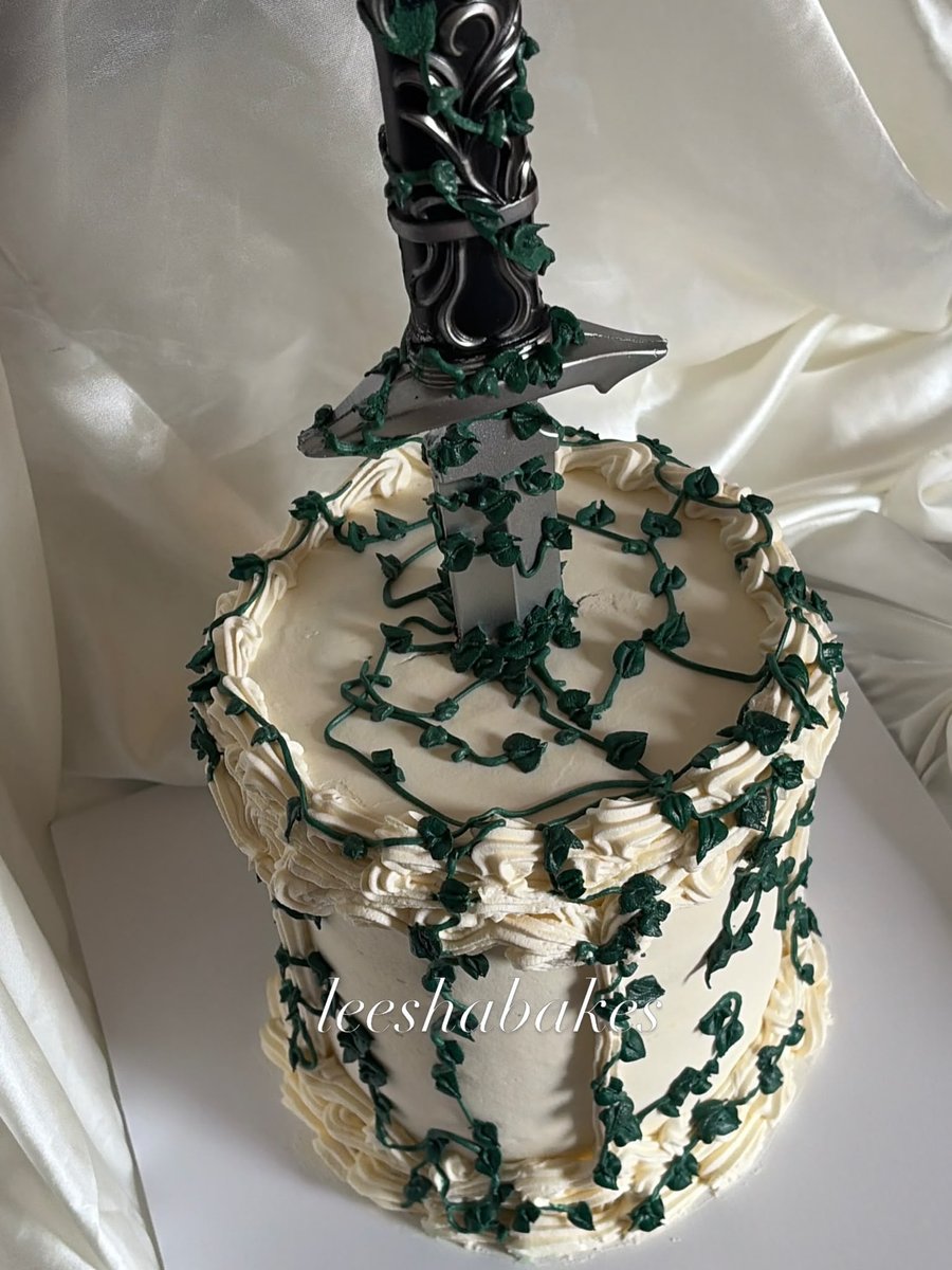 Cream rosette cake trailed with green ivy and a decorative dagger topper