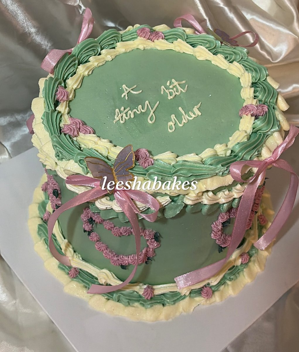 Green and cream vintage cake with pink piped flowers, bows and a butterfly reading 'a tiny bit older'