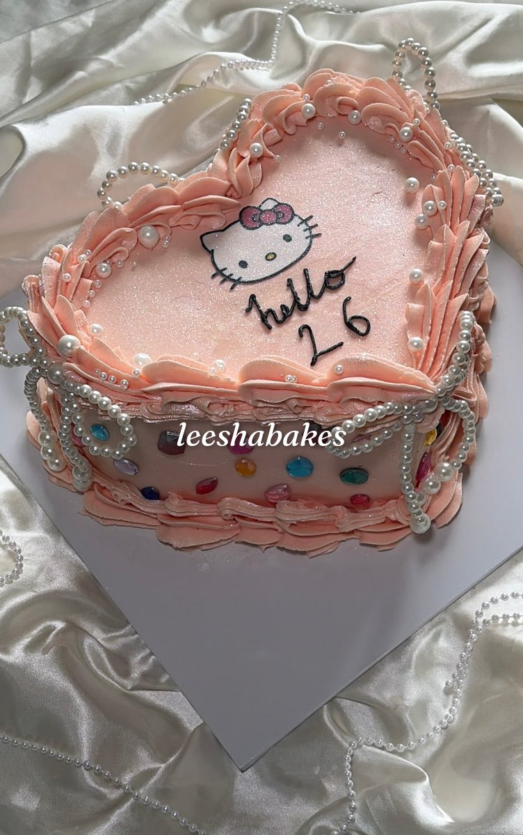 Peach heart cake with pearls, colourful gems and a Hello Kitty topper reading 'hello 26'