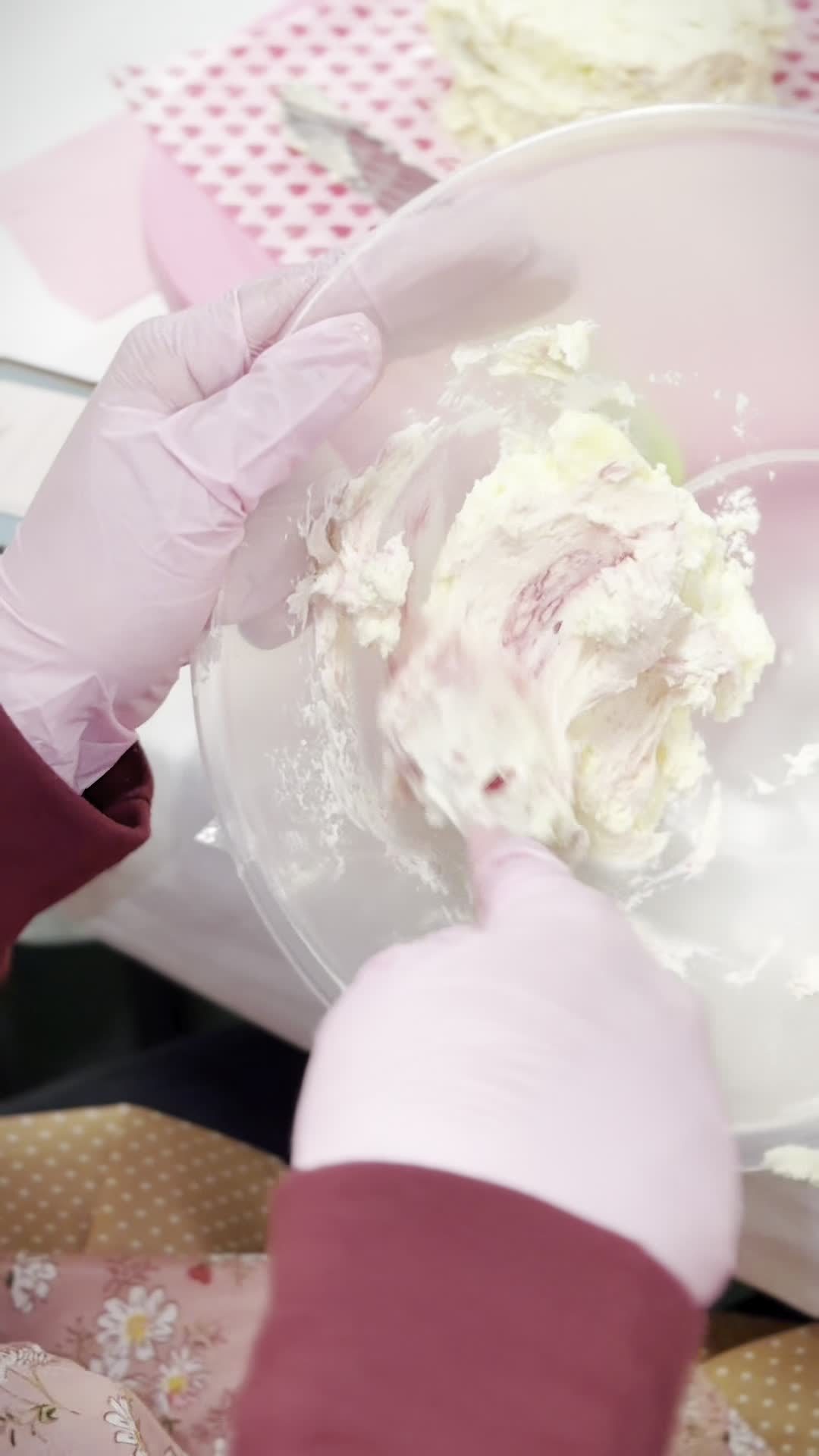 Pink-gloved hands mixing strawberry buttercream